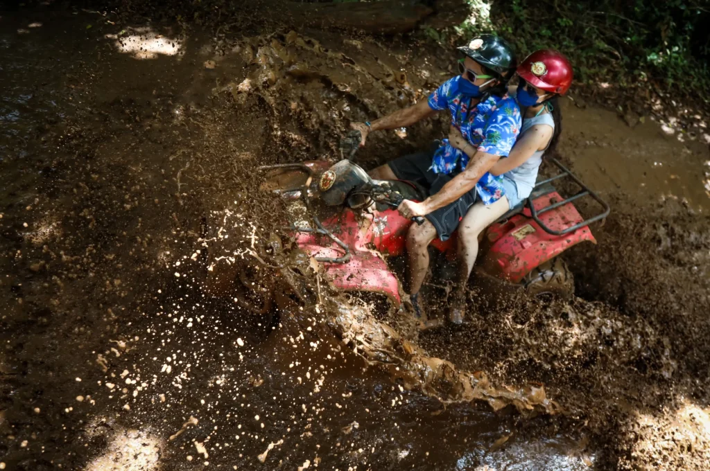 Two ATV riders splashing through a deep mud puddle in the Cancun jungle