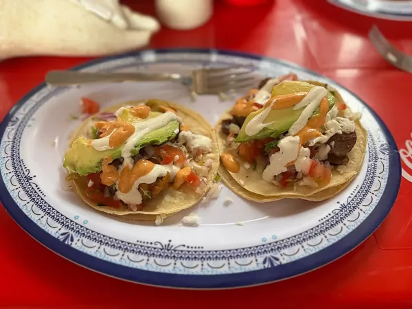 Two tacos loaded with fresh toppings, including avocado, salsa, and cream.