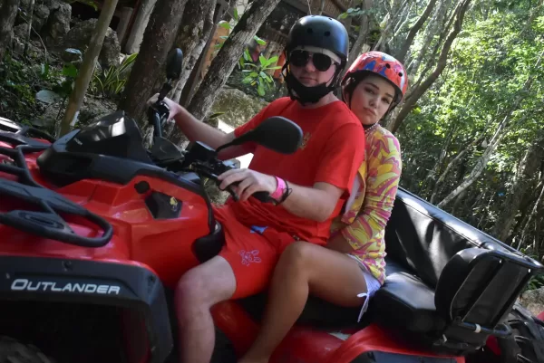 Couple riding a red ATV through a jungle trail during an adventure tour in Cancun.