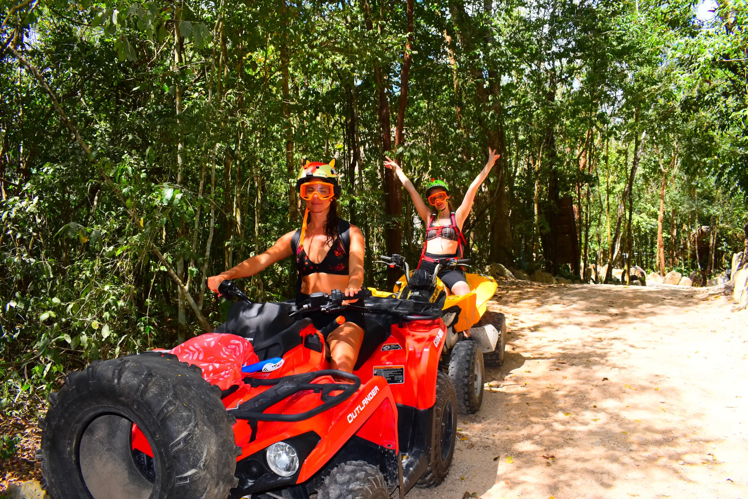 Two women celebrating while riding ATVs through the Cancun jungle.