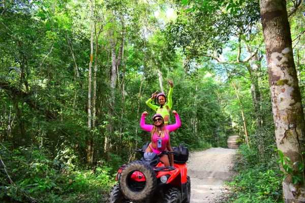 Two women posing victoriously on an ATV in the Cancun jungle.