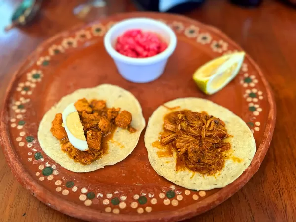 Two tacos with cochinita pibil and pickled onions on a traditional Mexican clay plate.