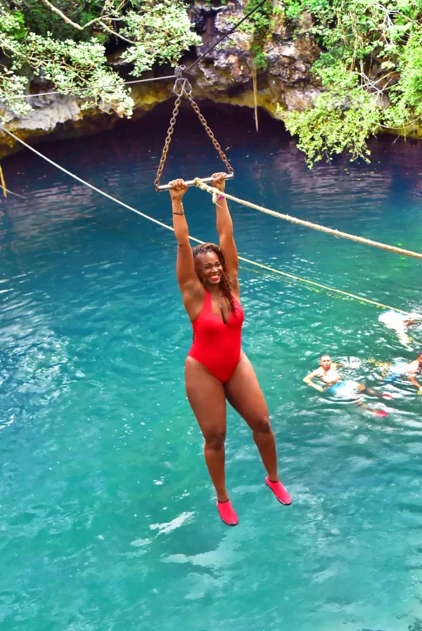 Woman in red swimsuit swinging on a rope over a crystal-clear cenote in Cancun.