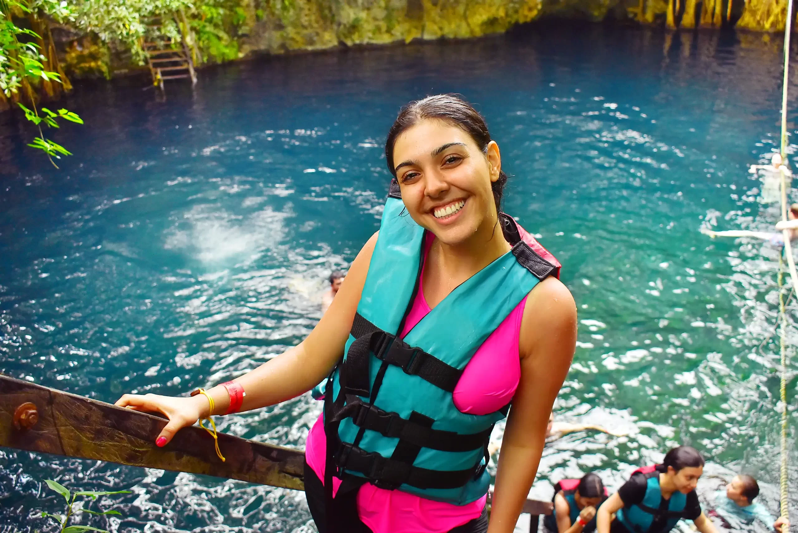 Smiling woman in a turquoise life jacket standing by a cenote in Cancun.
