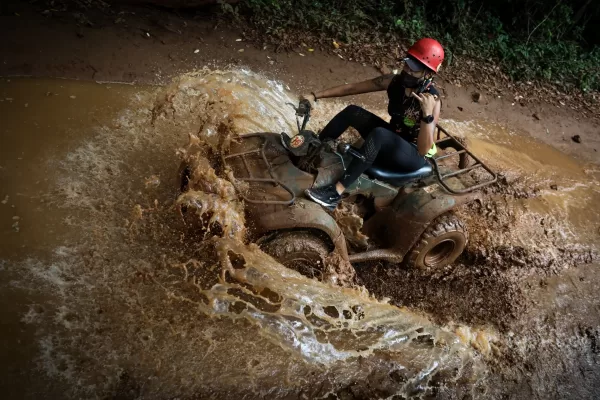 A solo rider maneuvering an ATV through muddy waters, creating a large splash while driving through Cancun's jungle terrain.