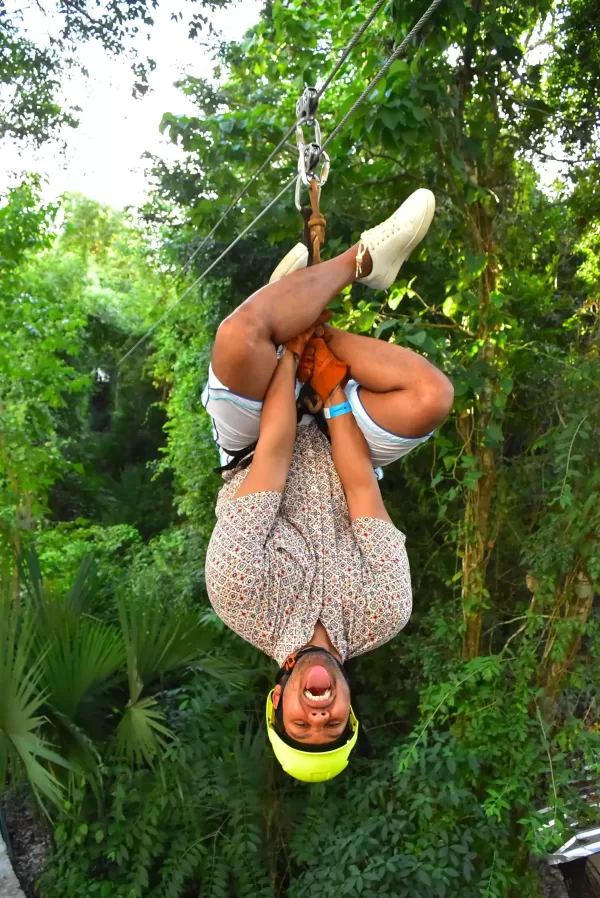 Man smiling and ziplining through a jungle, with trees and greenery in the background.