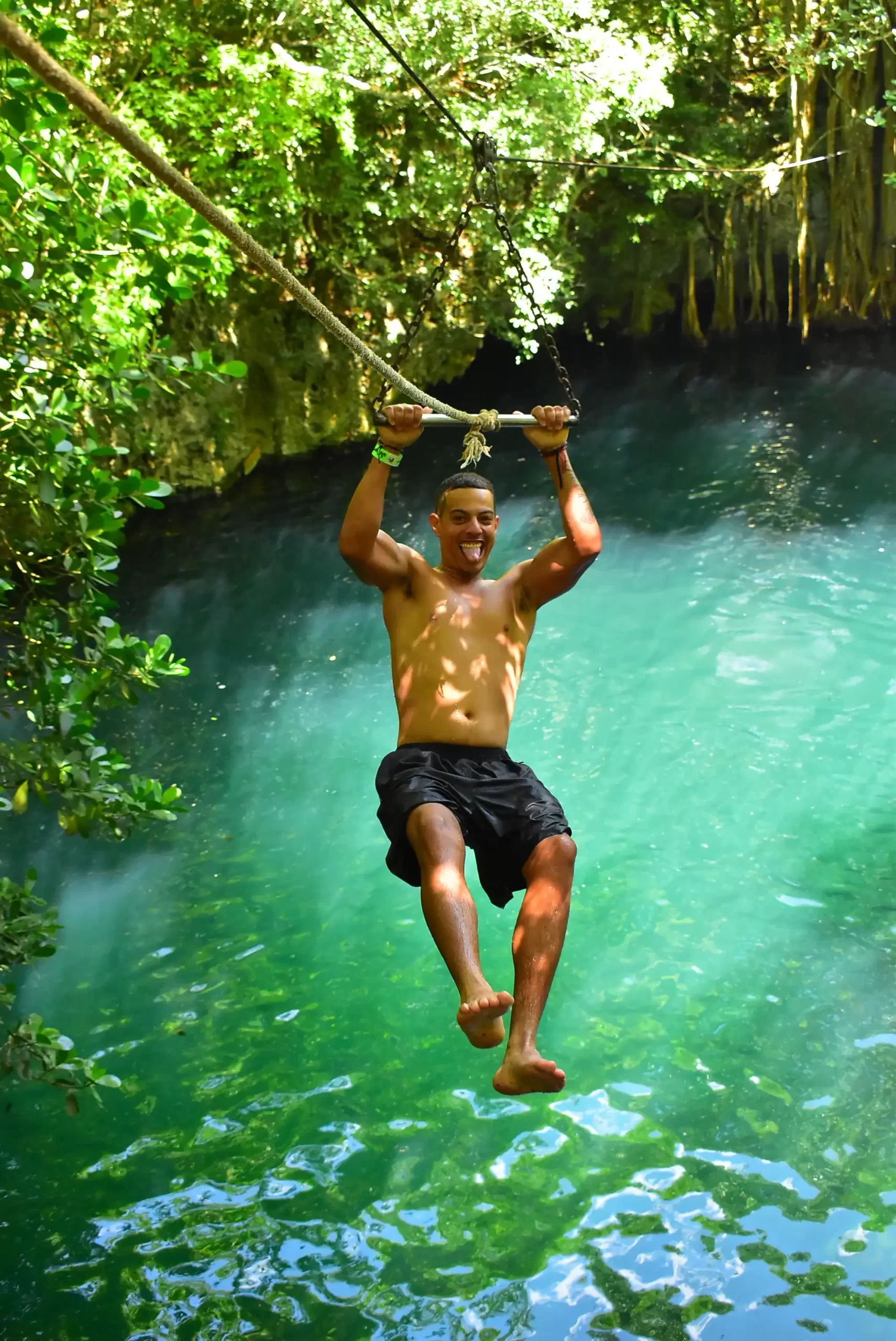 Man swinging over a cenote on a rope, about to drop into the water.