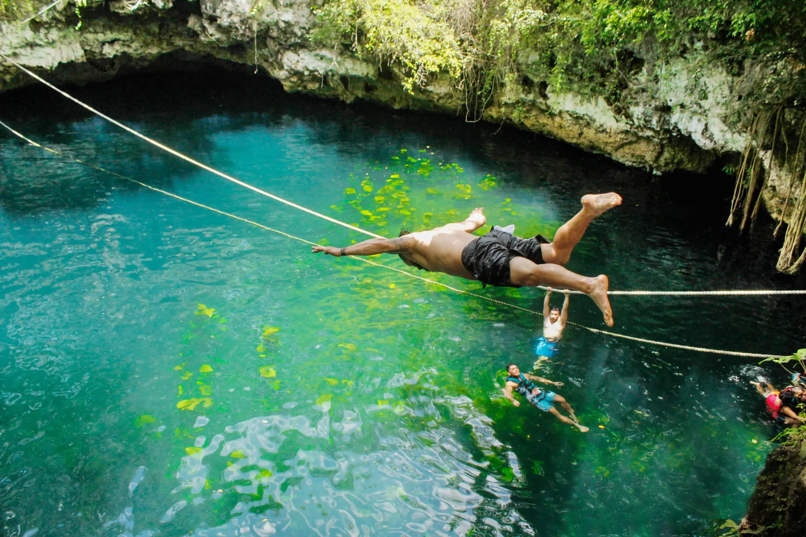 Man balancing on a rope above a cenote, preparing to fall into the water.