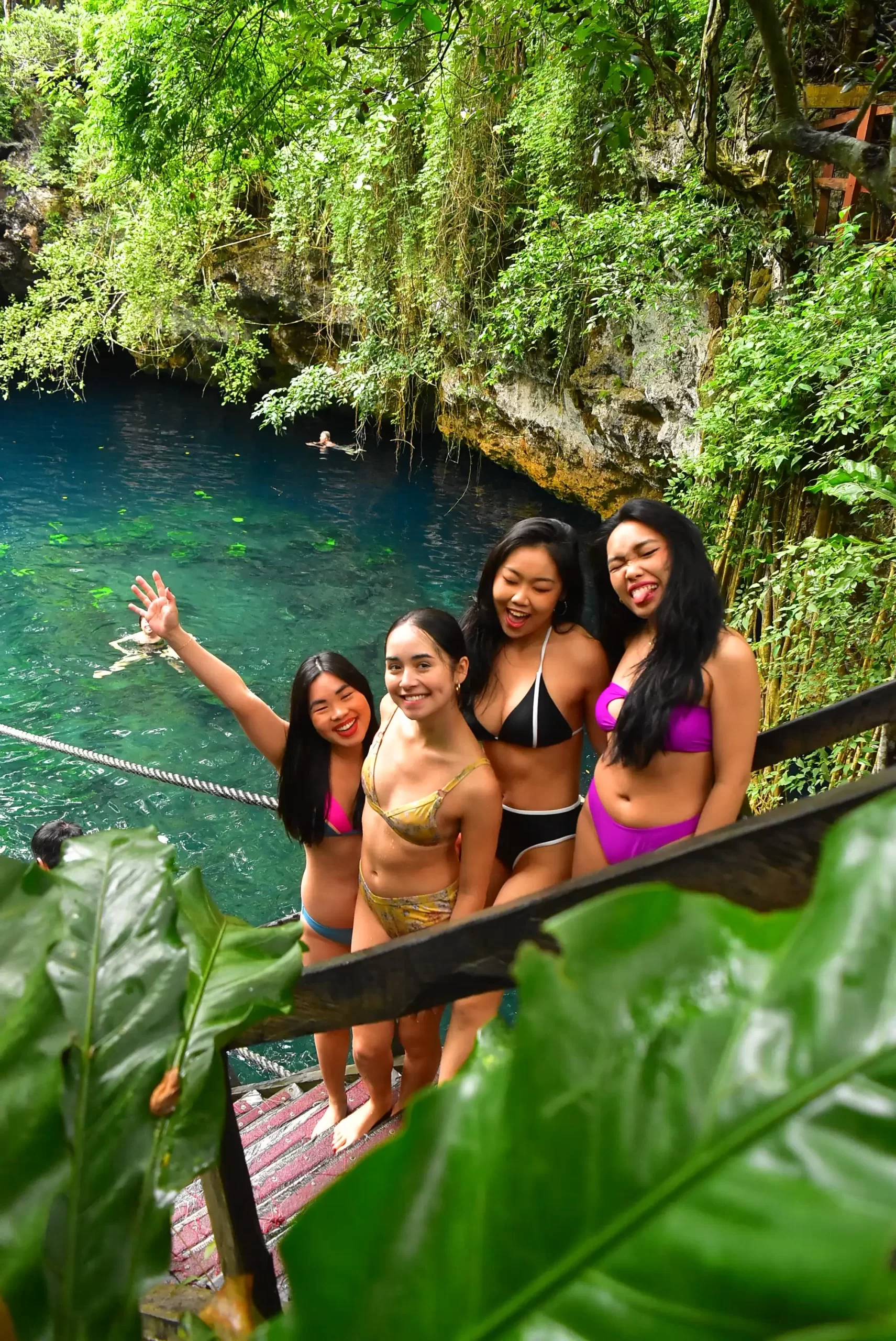 Group of friends in swimsuits posing by a cenote, smiling and enjoying their time near the water.