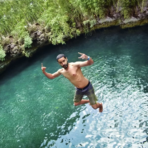 Man mid-jump into a cenote, making a peace sign with both hands, enjoying the water adventure