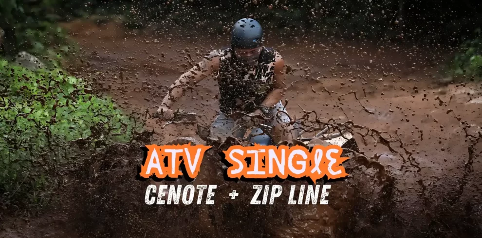Man riding a single ATV through mud on a jungle trail, splashing water and dirt.