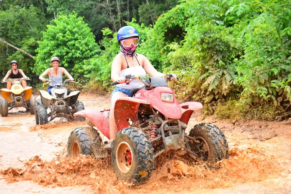 Woman riding an ATV through a muddy trail, followed by two other riders in the jungle