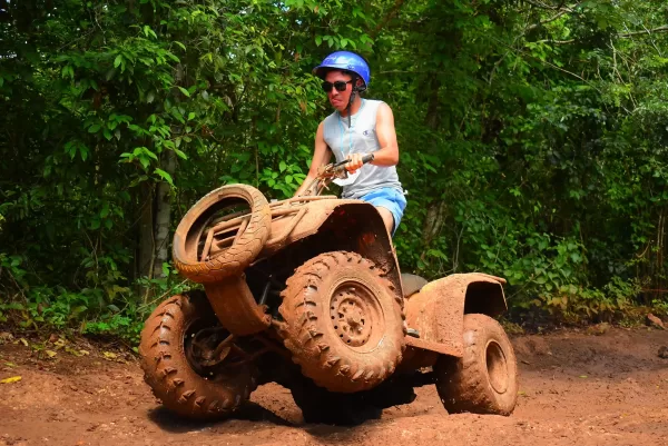 Man performing a wheelie on an ATV in the jungle, with the front wheels lifted off the ground.