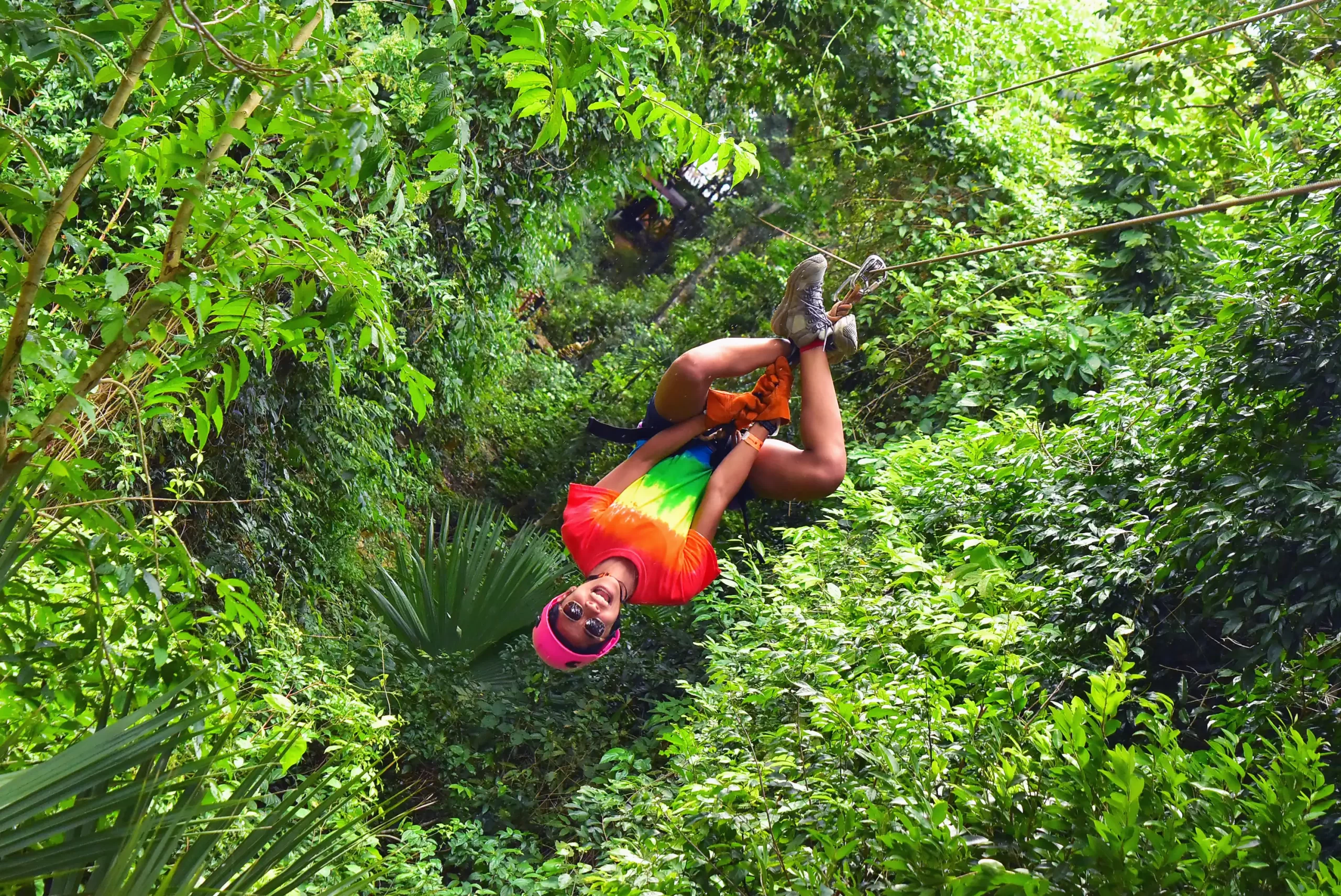 Woman ziplining upside down through the jungle, surrounded by dense greenery.