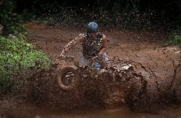 Person riding an ATV through a muddy trail, causing a large splash of mud around them.