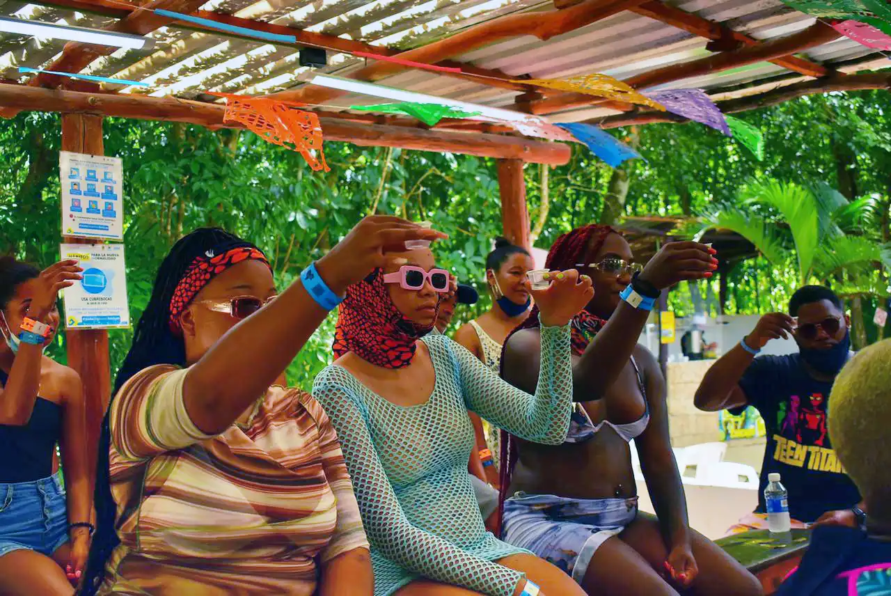 Group of people sitting under a shaded area taking tequila tasting during a break from activities.