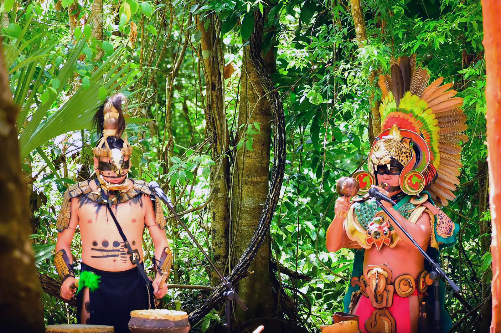 Mayan performers in ceremonial attire playing instruments in the jungle.