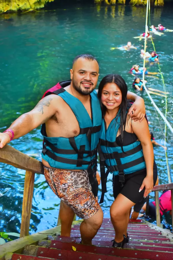 A couple wearing life jackets standing by the edge of a cenote, ready to enjoy a refreshing swim in the turquoise waters.