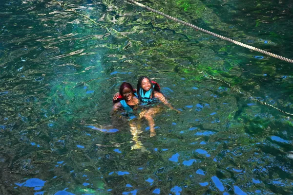 Two women in life jackets floating in a calm cenote, enjoying the crystal-clear waters and the peaceful atmosphere.