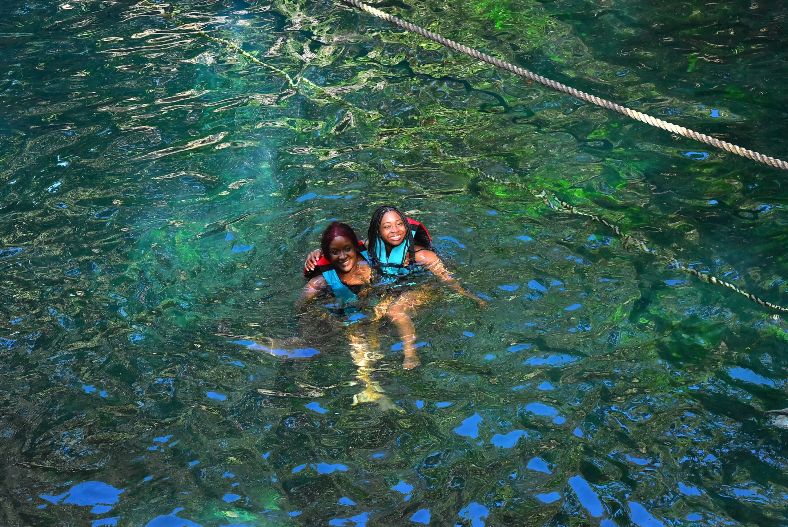 Two women in life jackets floating in a calm cenote, enjoying the crystal-clear waters and the peaceful atmosphere.