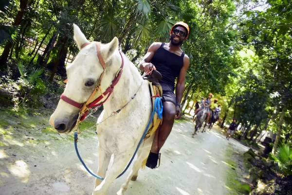 A person in black attire riding a white horse through the puerto morelos jungle