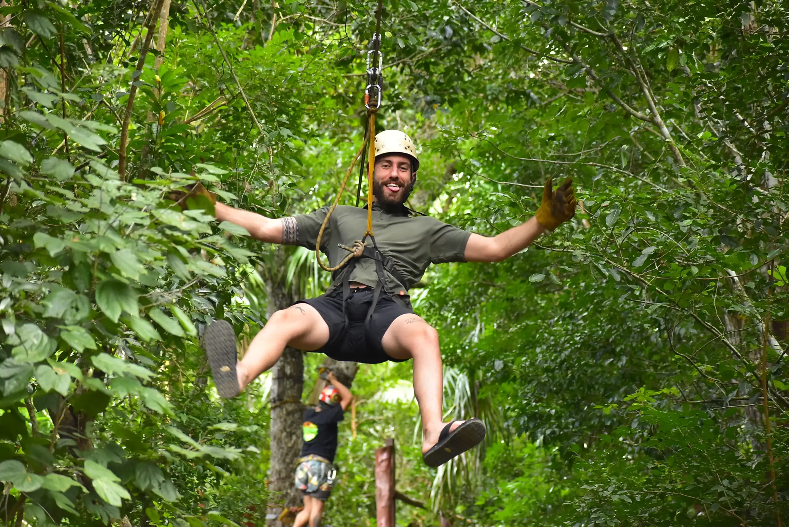 A man joyfully zip-lining through a lush forest, legs swinging mid-air.