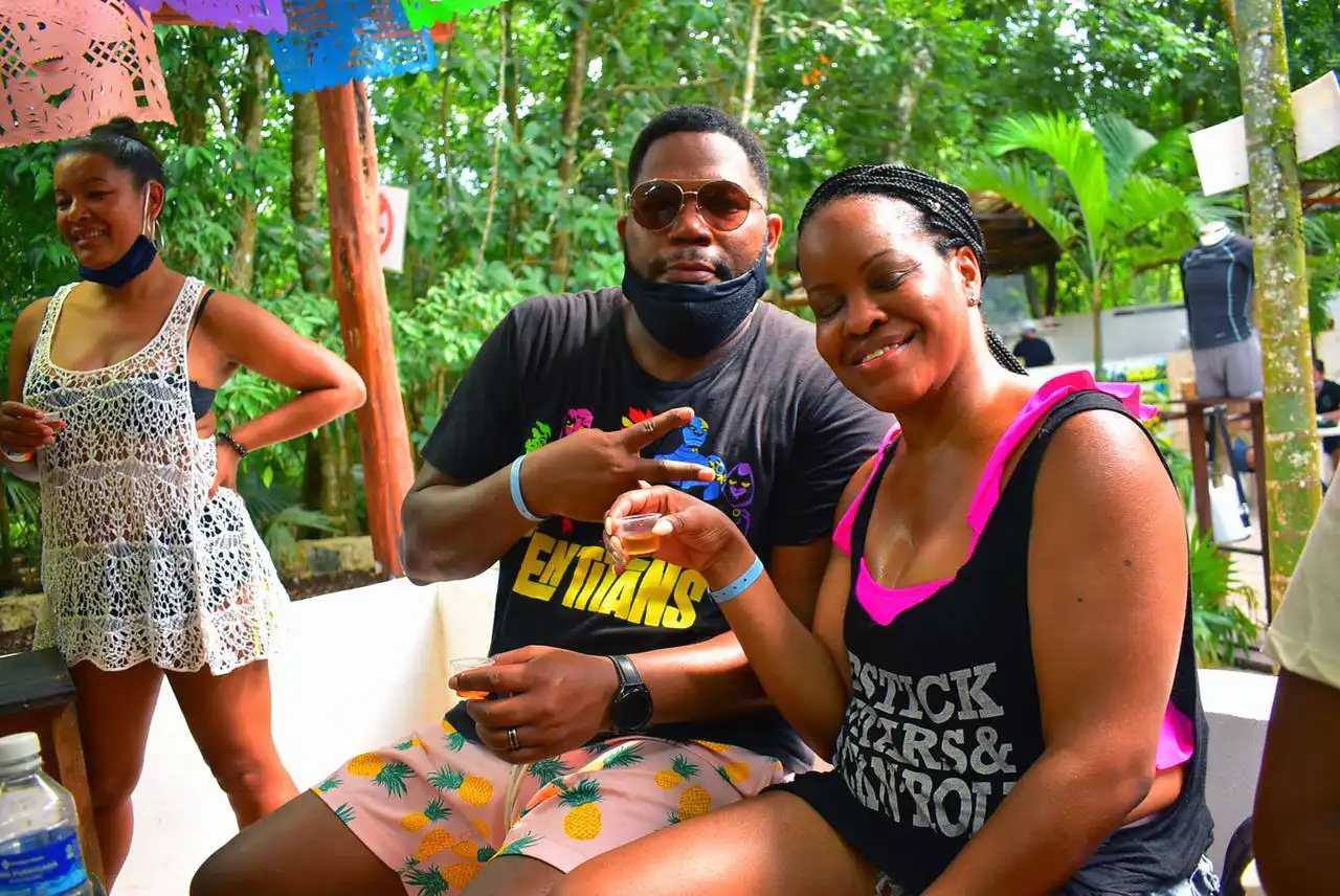 A man and a woman sit together enjoying tequila shots during a break from their outdoor adventure.