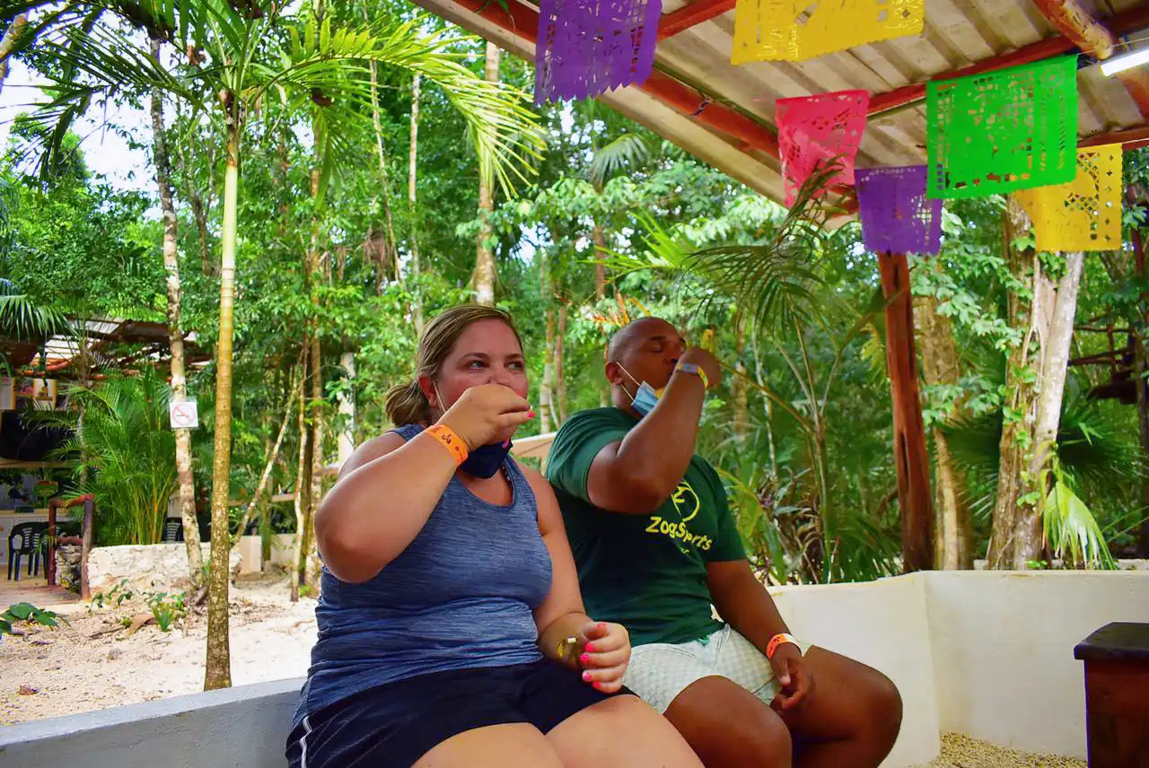Two friends taking a tequila shot together under a colorful, shaded outdoor setting.